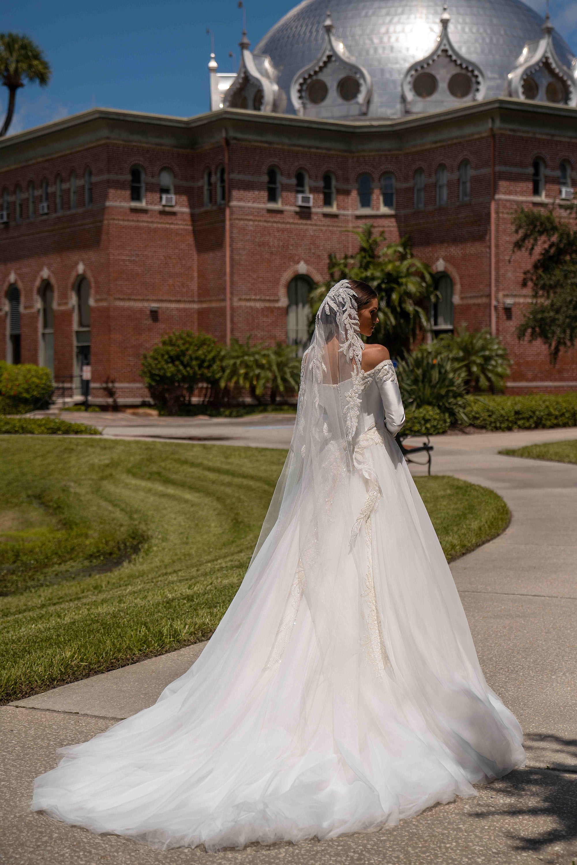 Back view of an ivory ball gown wedding dress with off-shoulder long sleeves, lace detailing, and a sweeping train