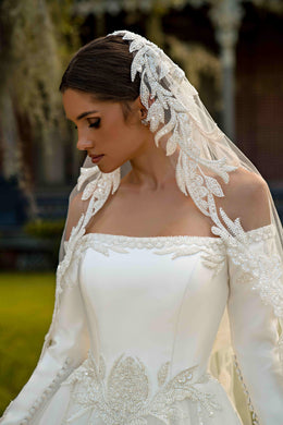 Close-up of an ivory wedding dress bodice with a square neckline, beaded floral appliqués, and sheer long sleeves
