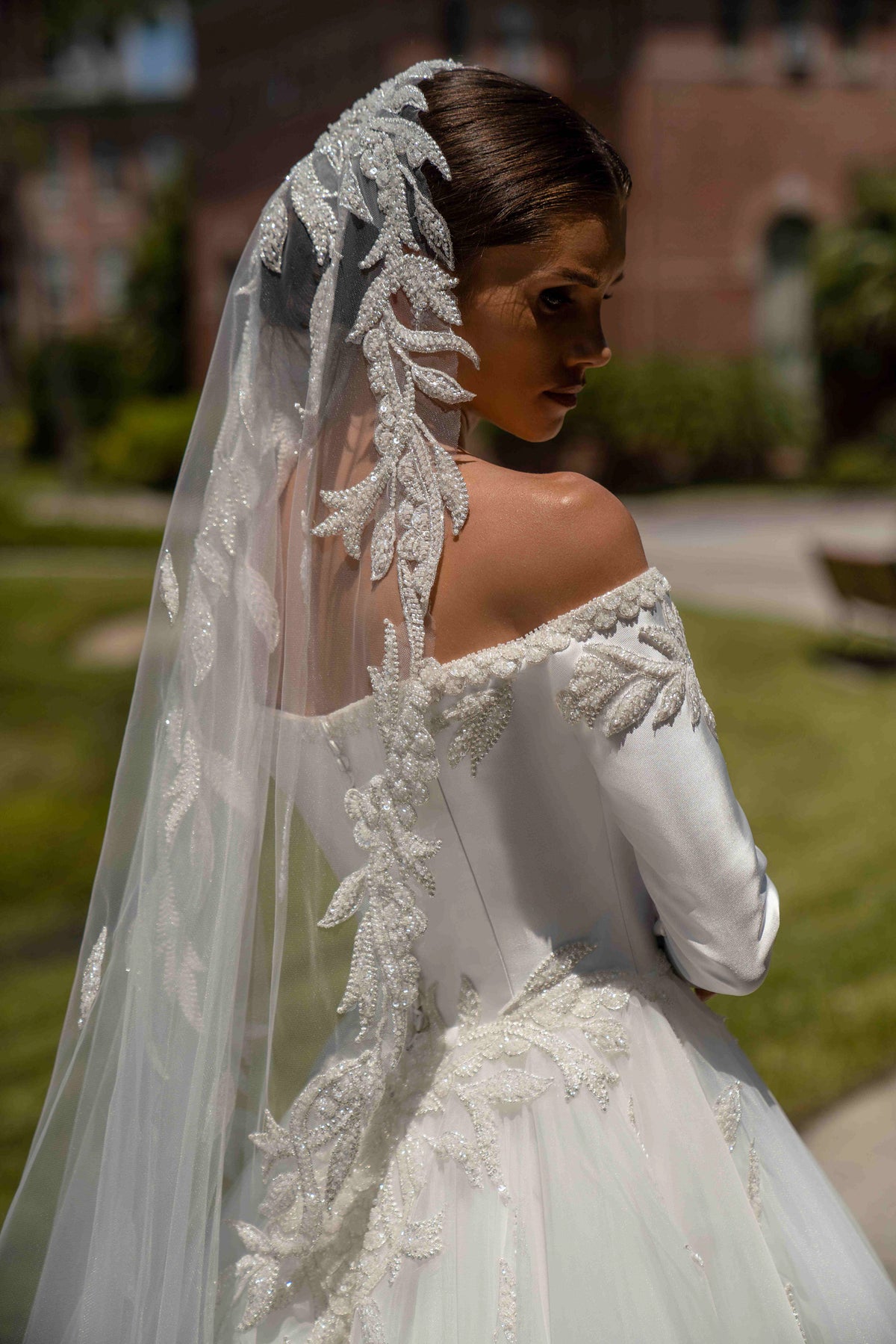 Ivory wedding dress showing the off-shoulder back, long sleeve, and cascading floral appliqués over the full skirt