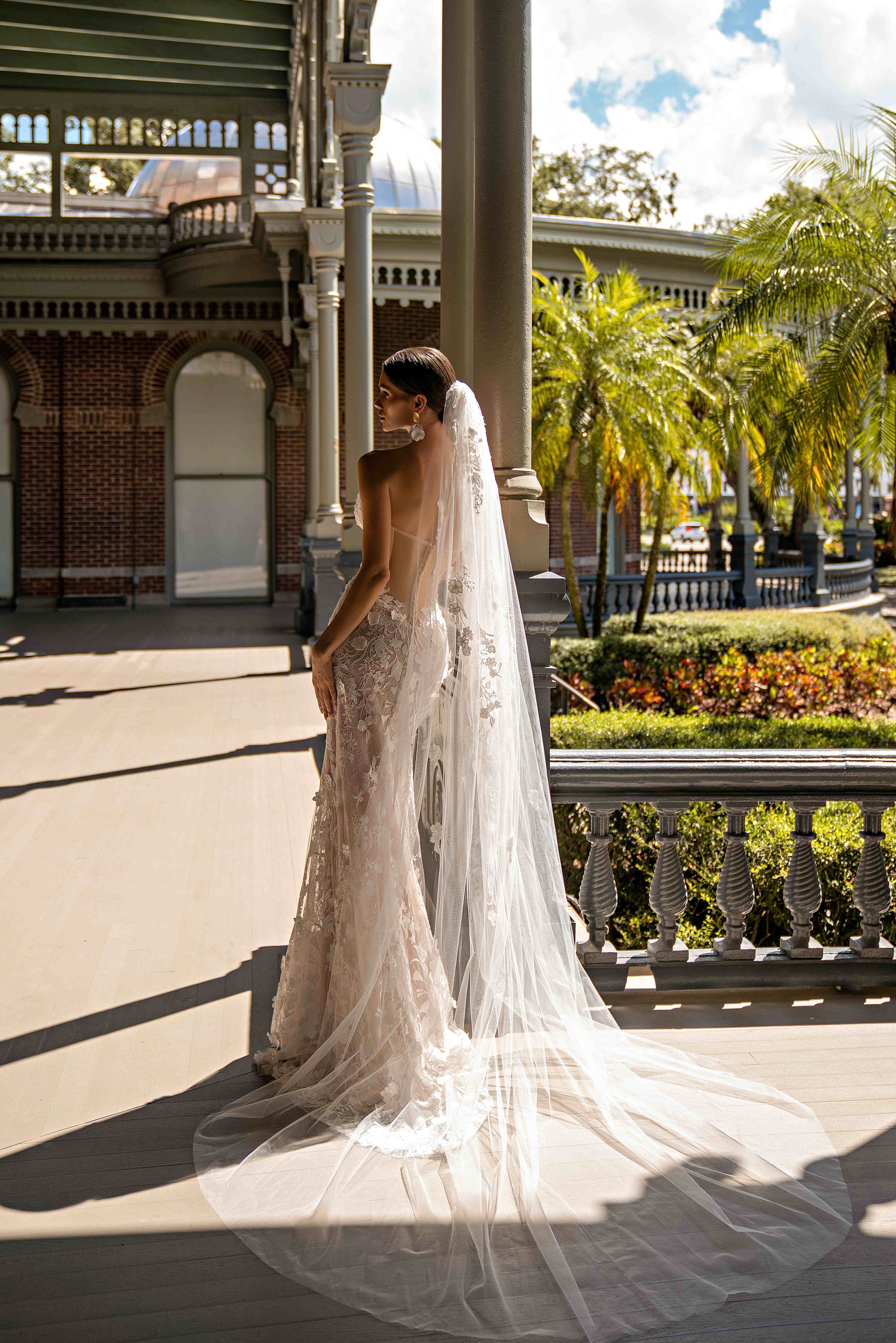 Side-back view of an ivory lace wedding dress with a fitted silhouette and long flowing train