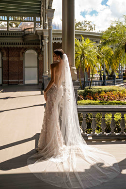 Side-back view of an ivory lace wedding dress with a fitted silhouette and long flowing train