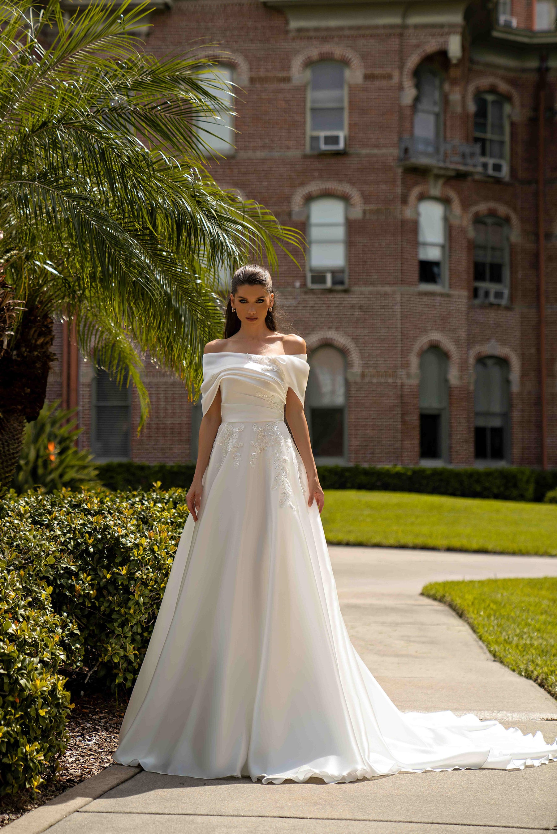 Ivory A-line wedding dress with an off-the-shoulder draped neckline, lace appliqués, and a long train