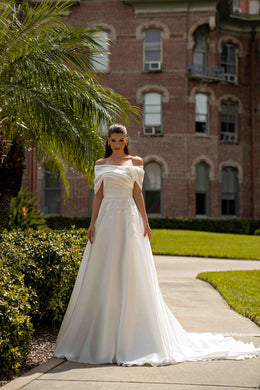 Ivory A-line wedding dress with an off-the-shoulder draped neckline, lace appliqués, and a long train