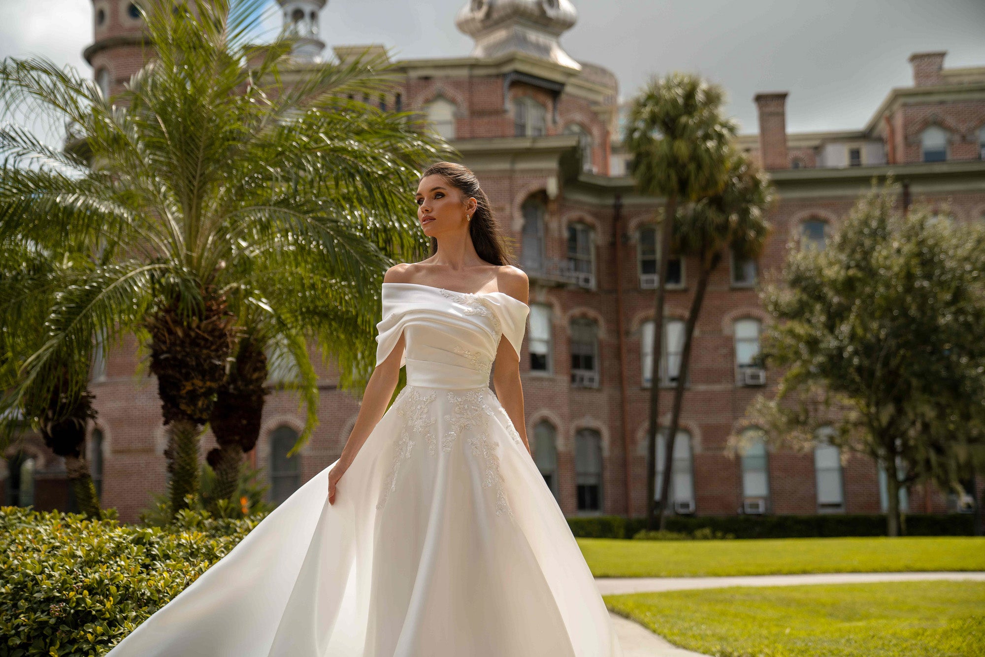 Ivory satin wedding dress with a draped off-the-shoulder neckline, fitted waist, lace appliqués, and flowing skirt