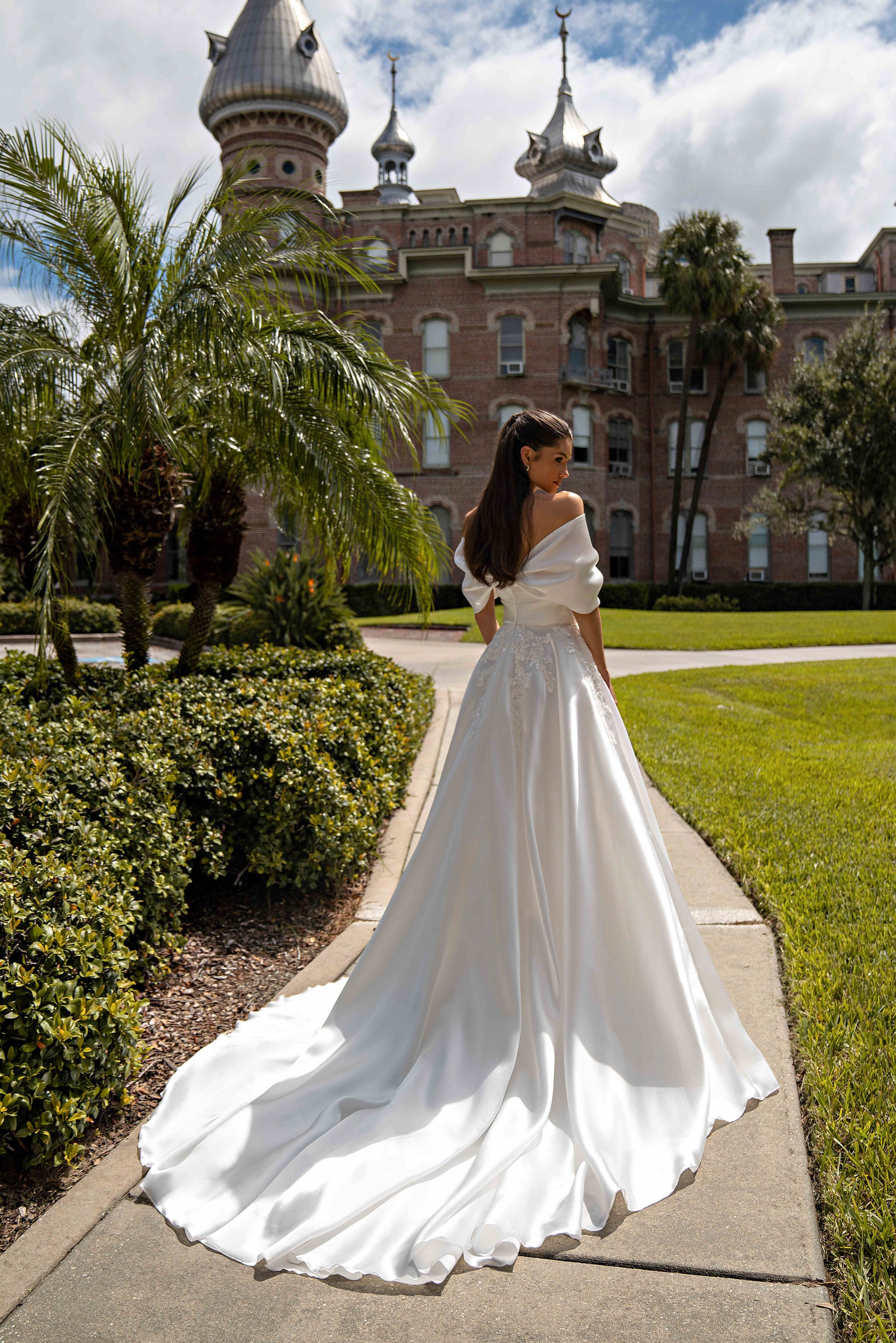 Back view of an ivory A-line wedding dress showing the draped neckline, lace-decorated waist, and sweeping train