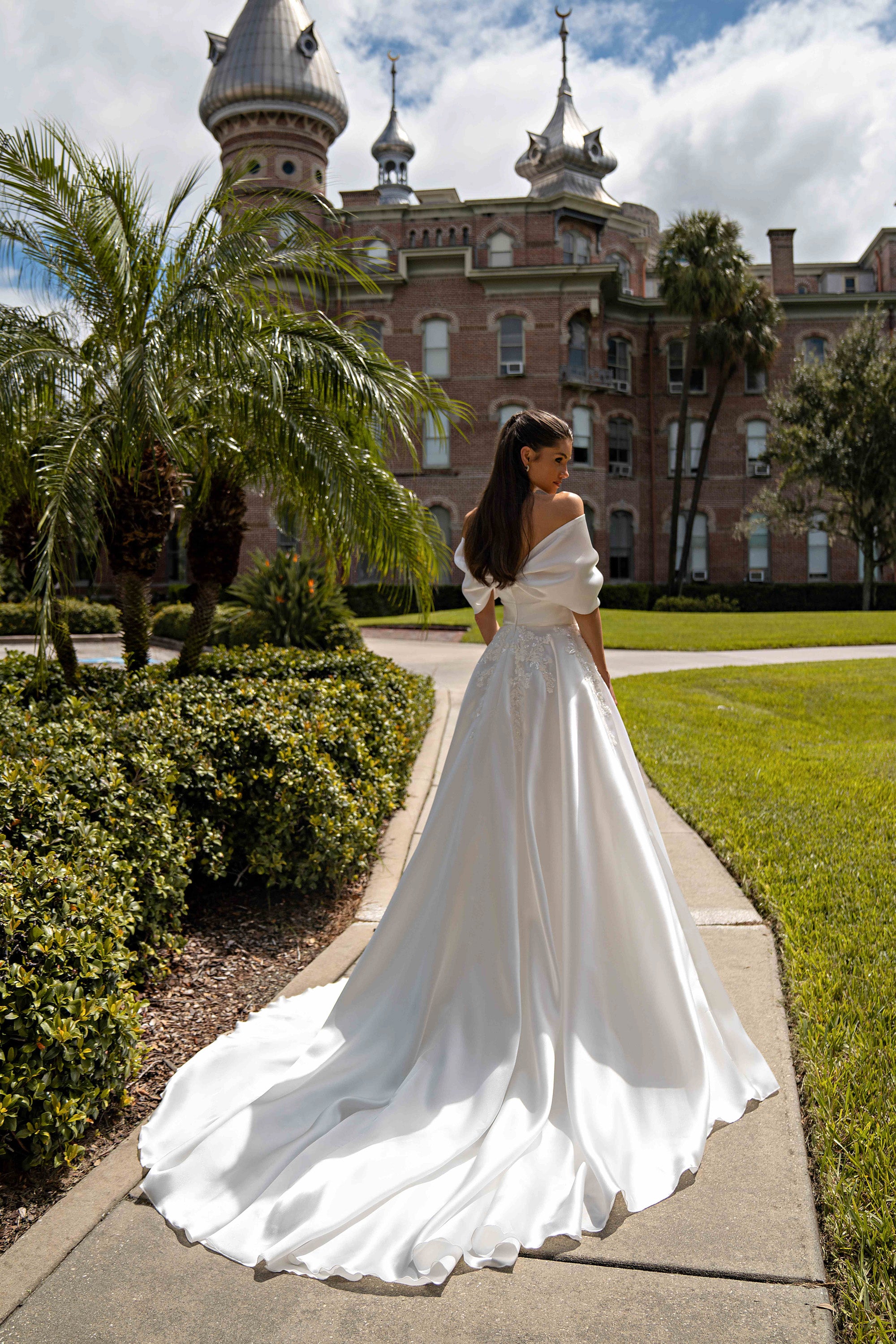 Back view of an ivory A-line wedding dress showing the draped neckline, lace-decorated waist, and sweeping train