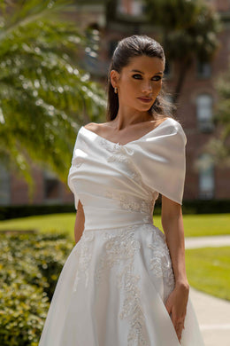 Close-up of an ivory wedding dress bodice with draped off-the-shoulder neckline and floral lace appliqués