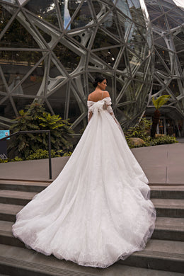 Ivory wedding dress with off-the-shoulder lace sleeves, a full glittering skirt, and long train