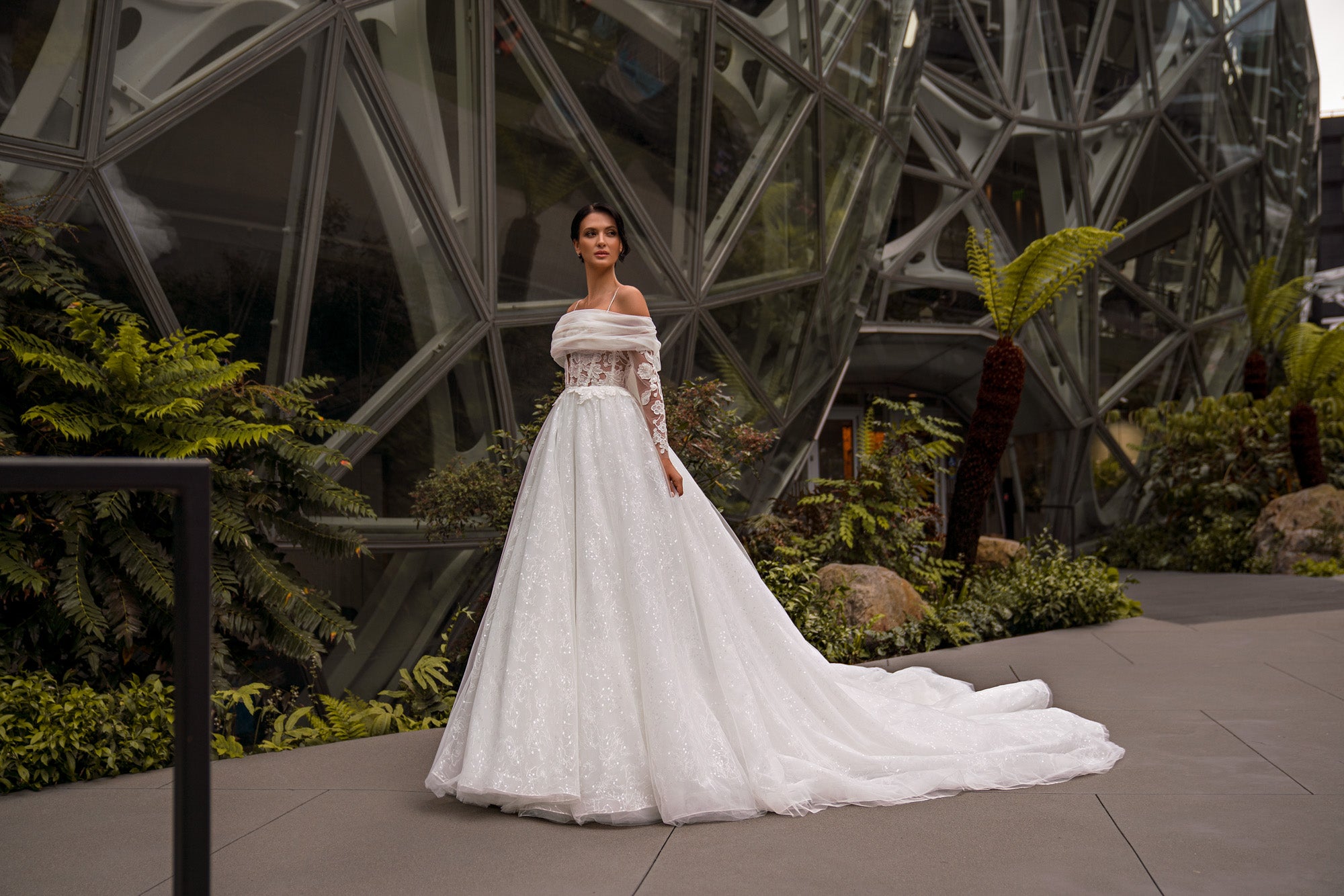Ivory A-line wedding dress featuring draped off-the-shoulder sleeves, a sparkling skirt, and extended train