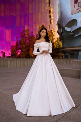 White ball gown wedding dress with a draped off-the-shoulder neckline, long sleeves, and a full skirt