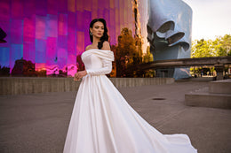 Angled white ball gown wedding dress with long sleeves, a draped neckline, and an extended train