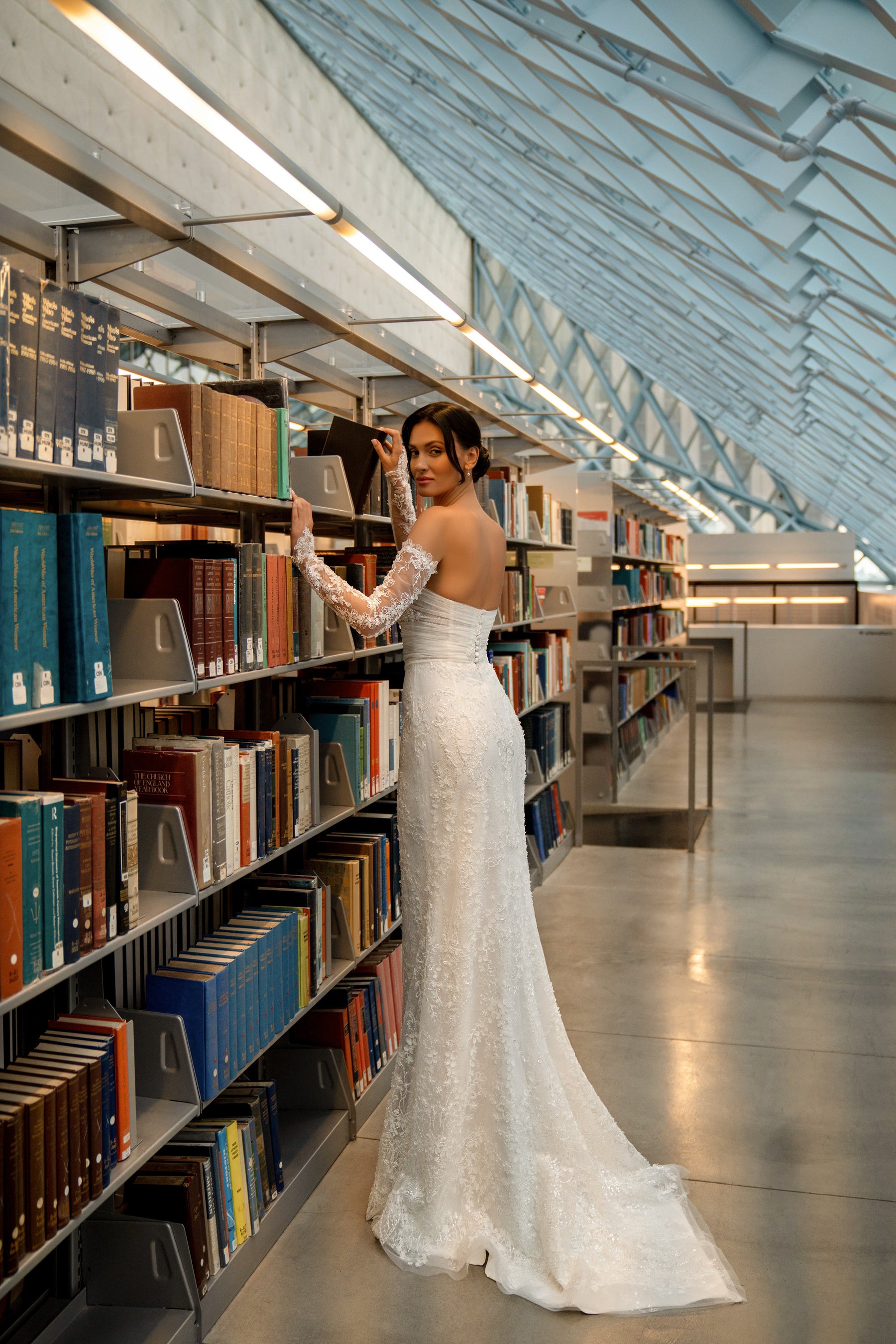 Ivory wedding dress showing a low open back, fitted mermaid silhouette, lace sleeve, and sweeping train