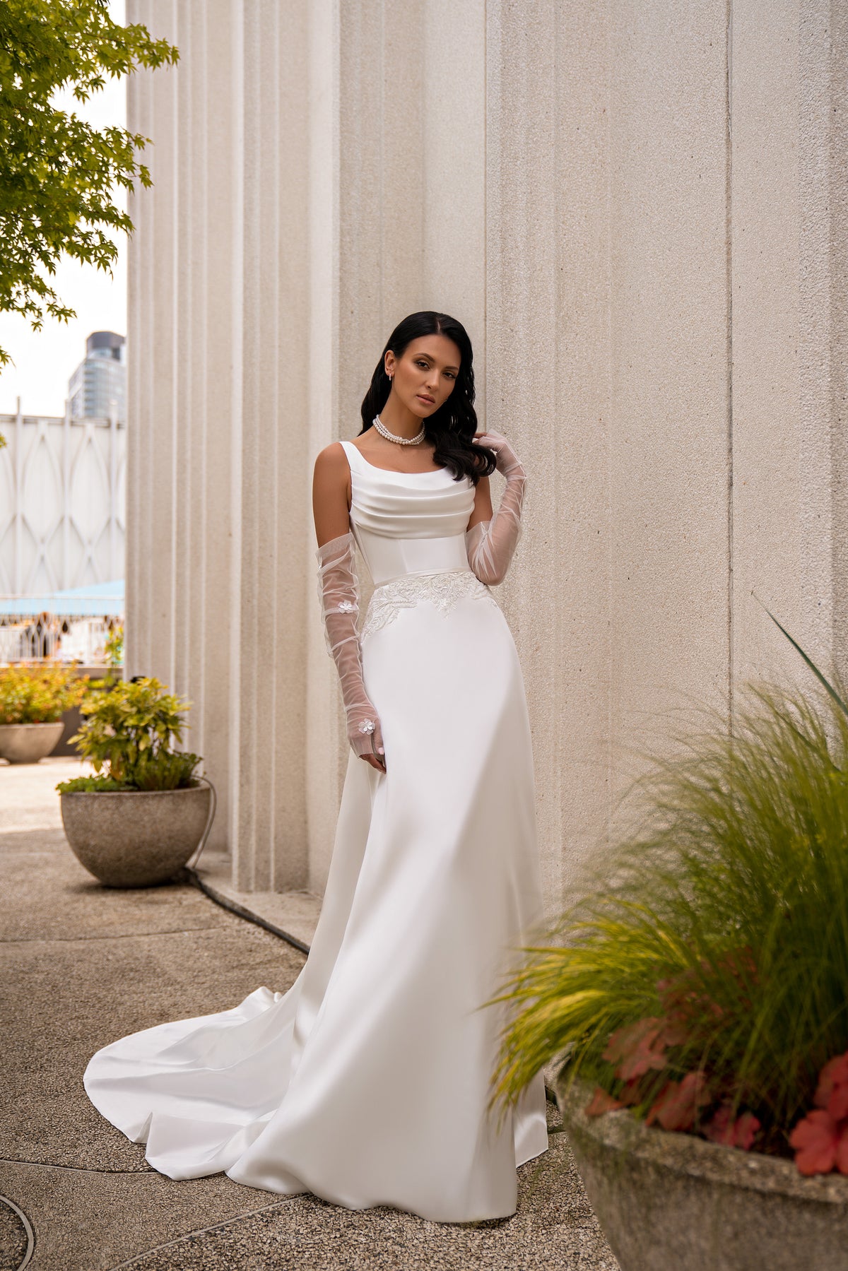 Ivory sheath wedding dress with draped scoop neckline, sheer sleeves, lace waist detail, and long train