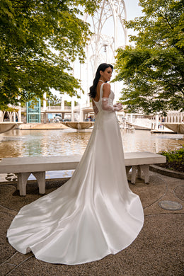 Ivory wedding dress showing its low back, sheer long sleeves, fitted bodice, and sweeping satin train