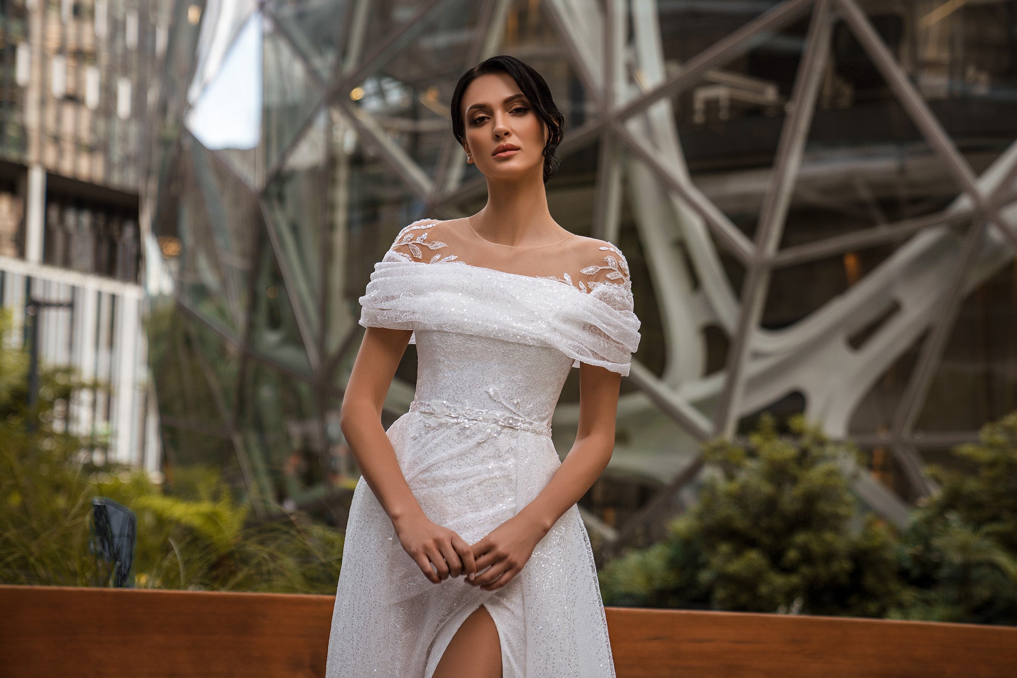 Close-up of an ivory wedding dress with lace shoulder details, an off-the-shoulder neckline, and high slit