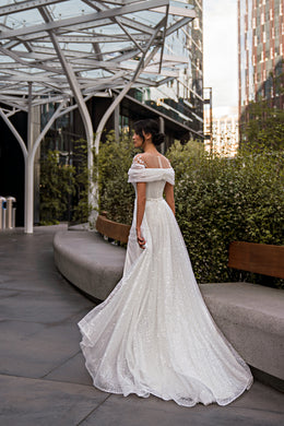 Rear three-quarter view of an ivory wedding dress with an off-the-shoulder bodice and wide train