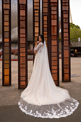Ivory wedding dress with a flowing sheer cape, lace detailing, and a wide train