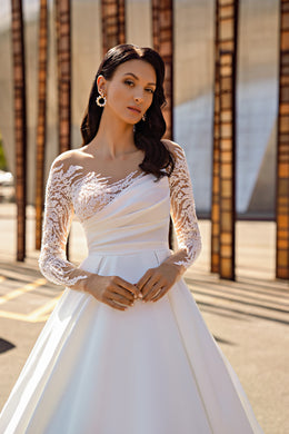 Close-up of an ivory wedding dress with a draped asymmetric neckline and sheer floral lace sleeves