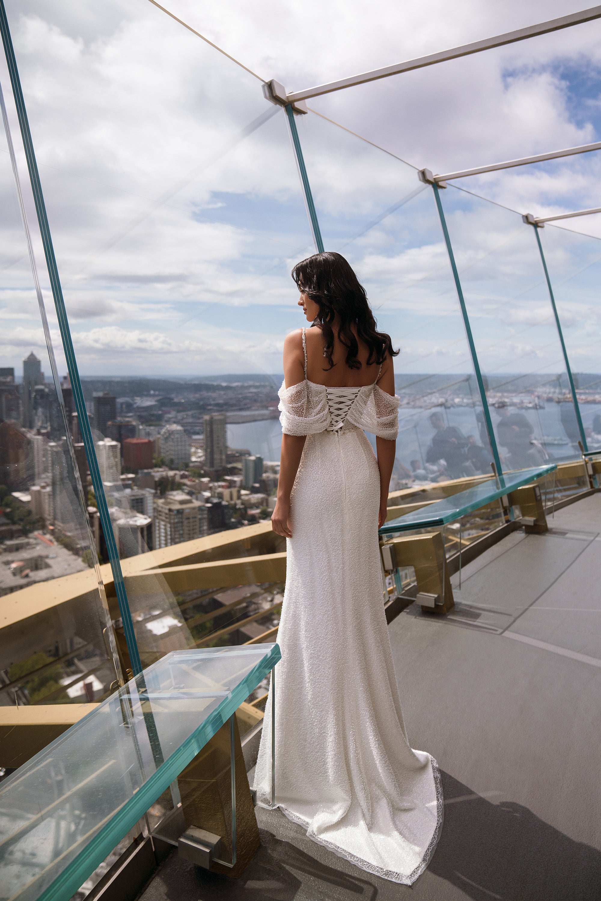 Back view of an ivory sheath wedding dress with off-the-shoulder sleeves and a long trailing train
