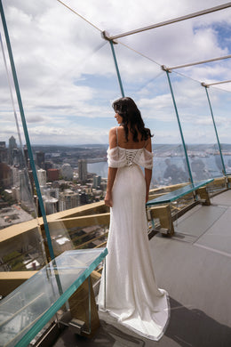 Back view of an ivory sheath wedding dress with off-the-shoulder sleeves and a long trailing train