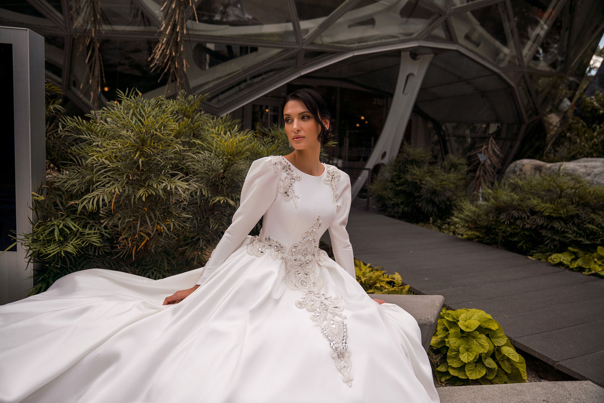 Ivory wedding dress with a round neckline, long sleeves, and ornate beaded appliqués on the bodice