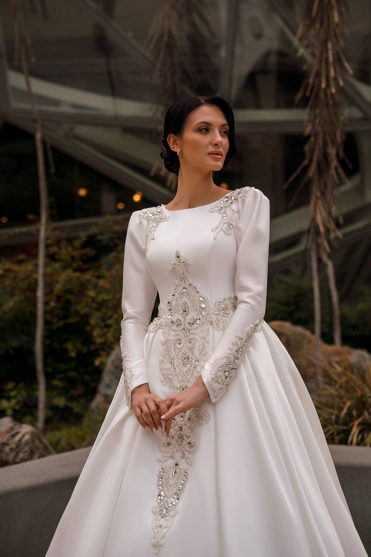 Close-up of an ivory wedding dress with long sleeves, a high neckline, and intricate beaded appliqués
