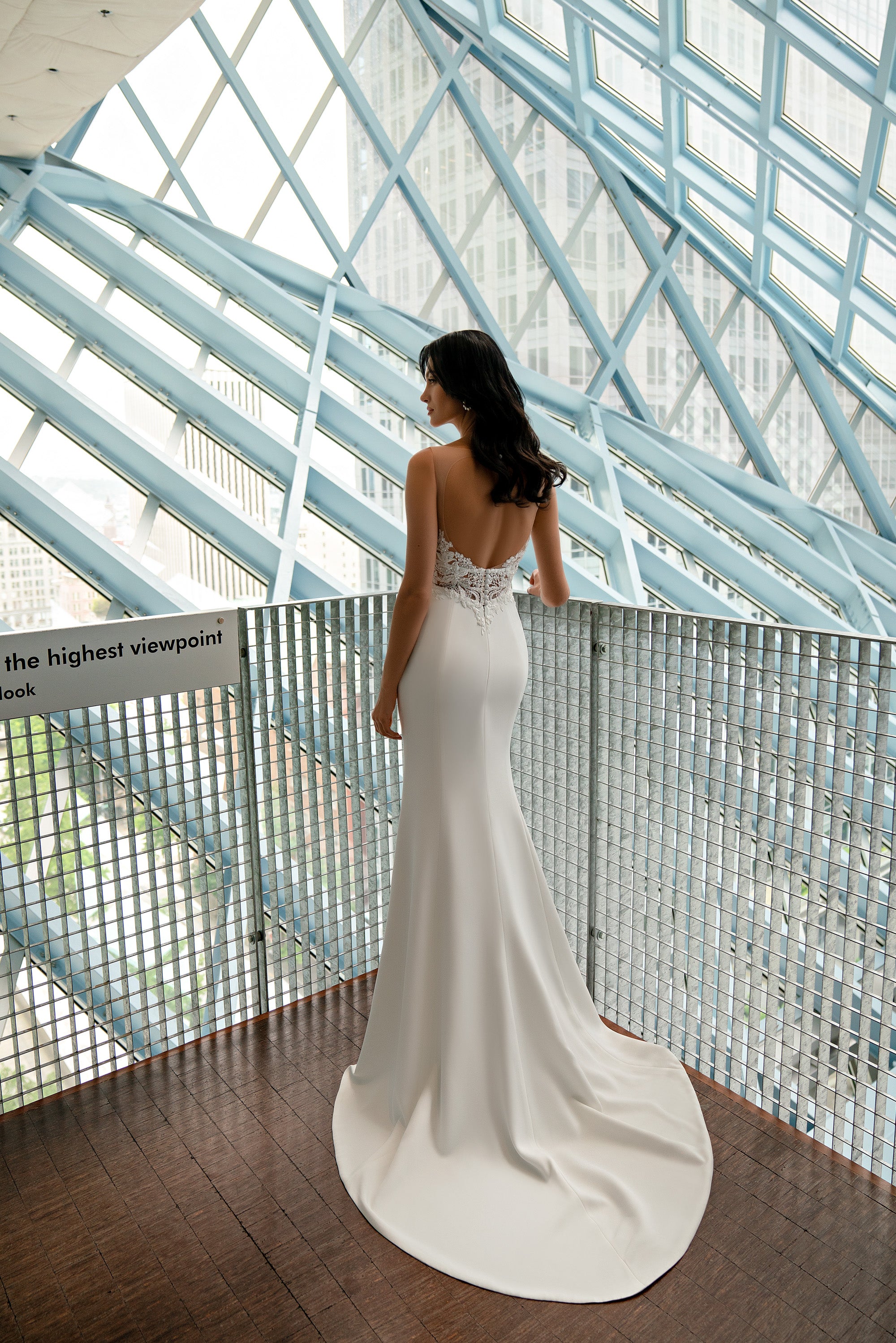 Open-back ivory sheath wedding dress with a lace waist panel and long trailing train