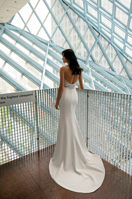 Open-back ivory sheath wedding dress with a lace waist panel and long trailing train