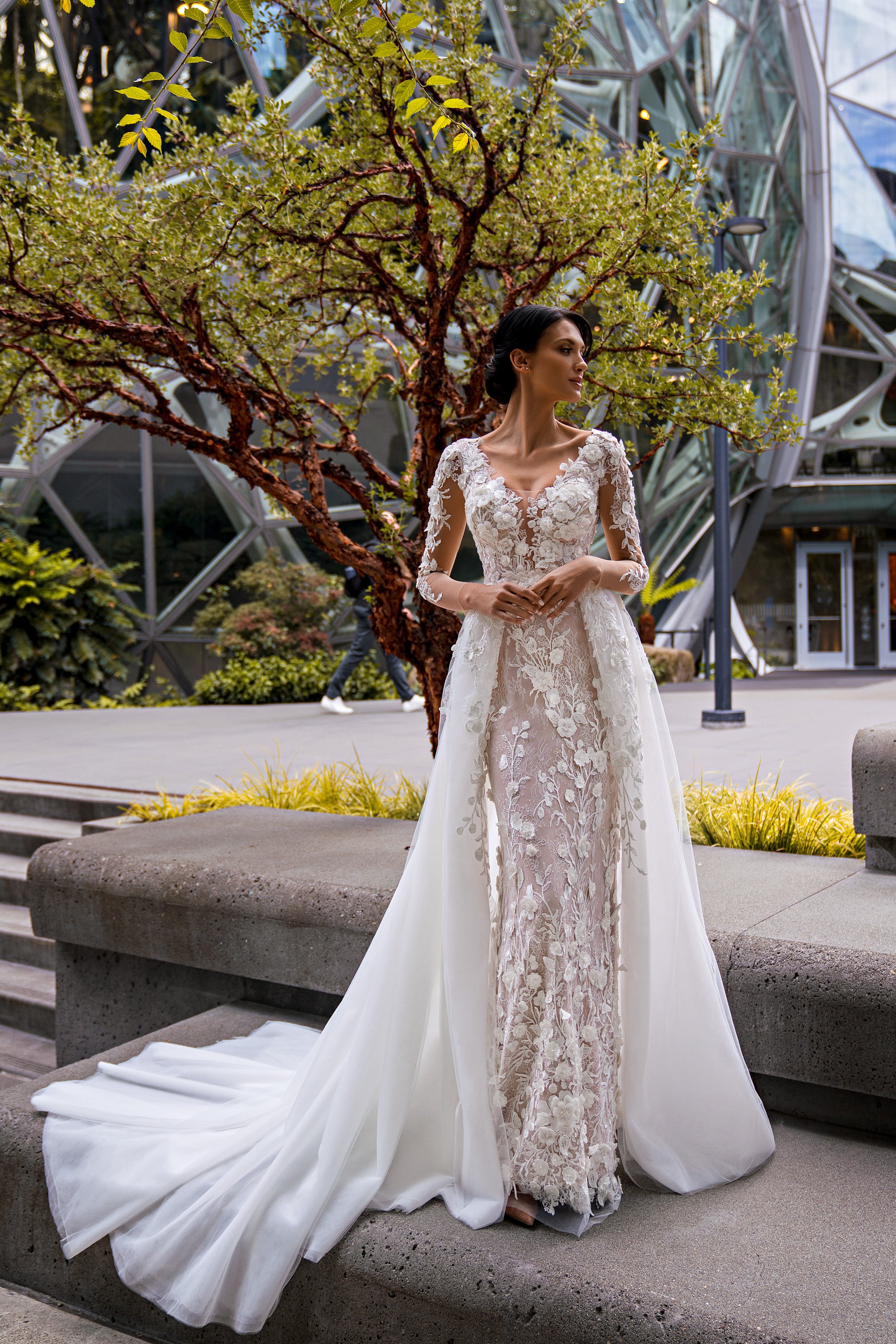 Ivory sheath wedding dress with floral lace, sheer long sleeves, and a flowing overskirt and train