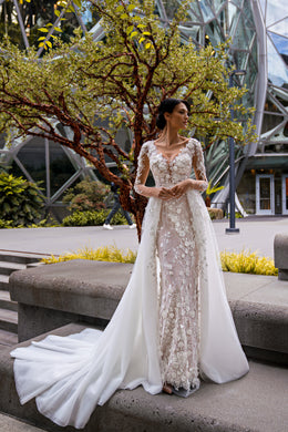 Ivory sheath wedding dress with floral lace, sheer long sleeves, and a flowing overskirt and train
