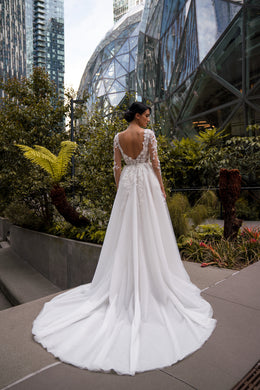 Open V-back wedding dress with lace sleeves, a full flowing overskirt, and a long train
