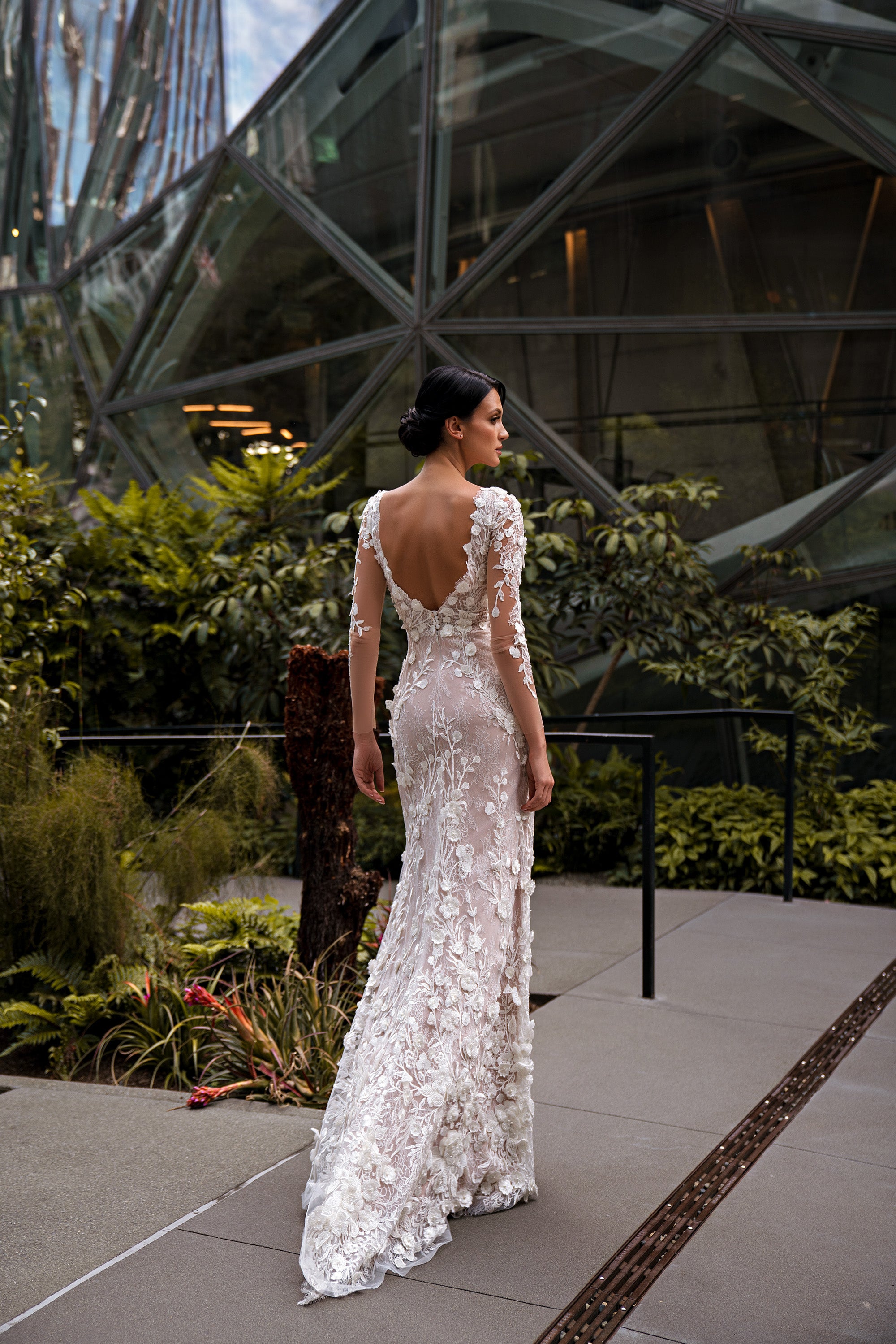 Sheath wedding dress with an open V-back, long lace sleeves, floral lace, and a trailing train
