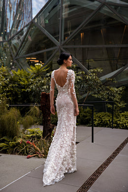 Sheath wedding dress with an open V-back, long lace sleeves, floral lace, and a trailing train