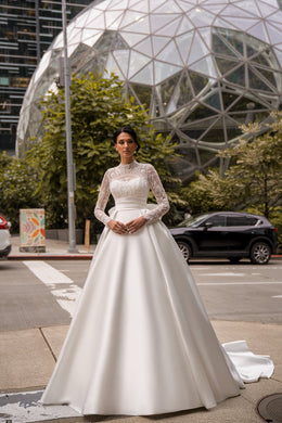 Ivory ball gown wedding dress with a high lace neckline, long sheer sleeves, and a full skirt with train