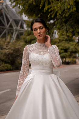 Close-up of an ivory wedding dress with a sheer lace high neckline, beaded floral bodice, and long sleeves