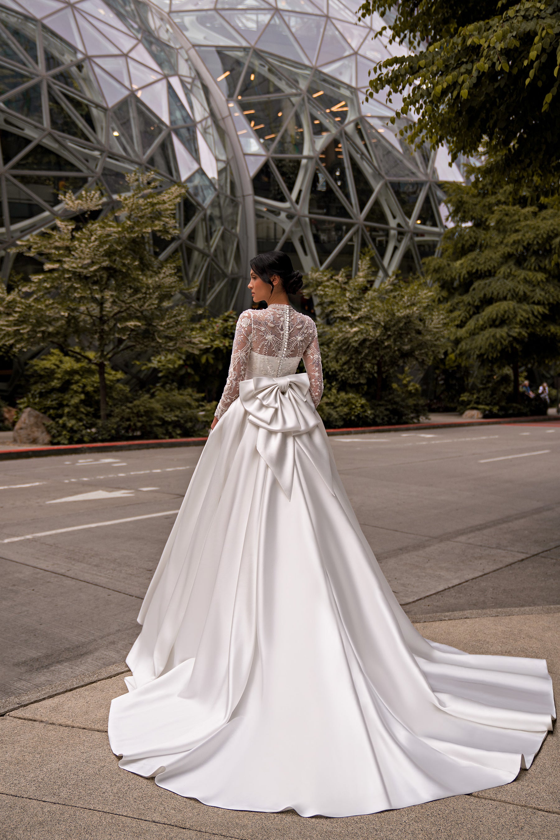 Back of an ivory wedding dress with an illusion lace bodice, oversized waist bow, and sweeping layered train