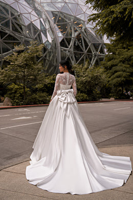 Back of an ivory wedding dress with an illusion lace bodice, oversized waist bow, and sweeping layered train