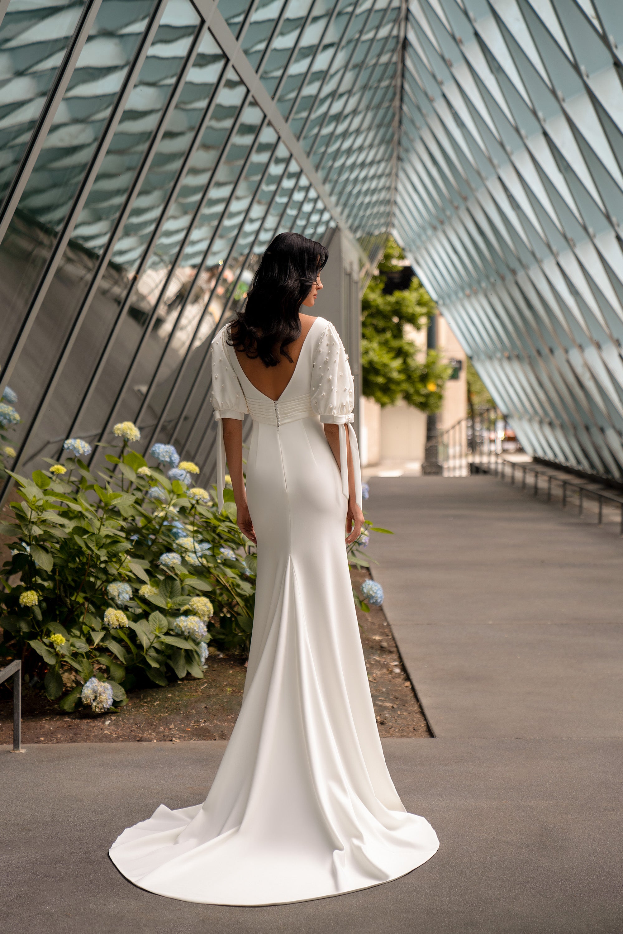 V-back ivory wedding dress with covered buttons, short sleeves, a fitted silhouette, and long train