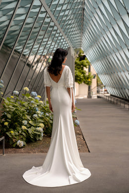 V-back ivory wedding dress with covered buttons, short sleeves, a fitted silhouette, and long train
