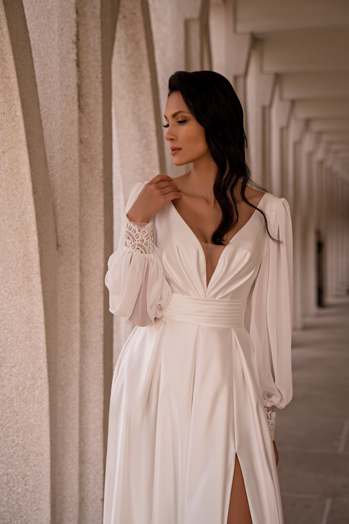 Close-up of an ivory wedding dress with a plunging V-neck, gathered waist, bishop sleeves, and lace cuffs