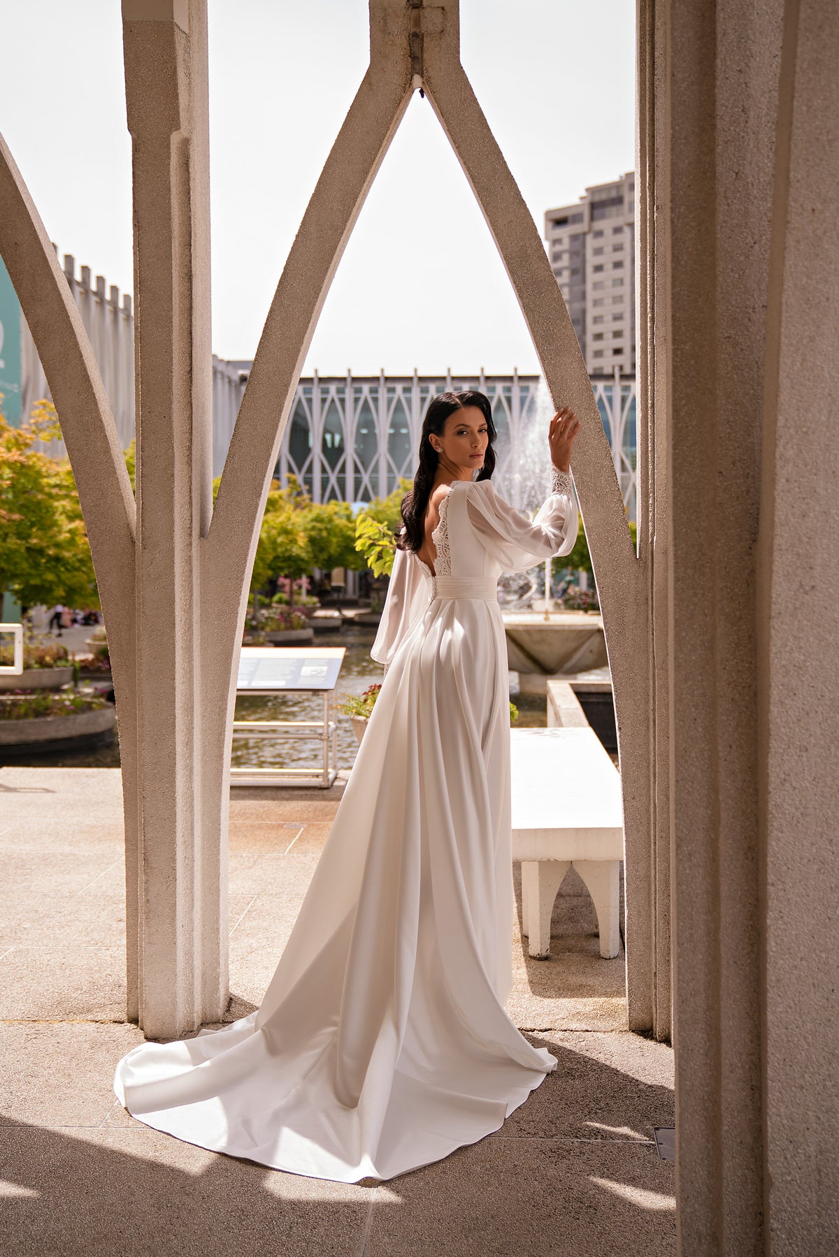Rear view of an ivory wedding dress showing long sleeves, a defined waist, flowing skirt, and long train