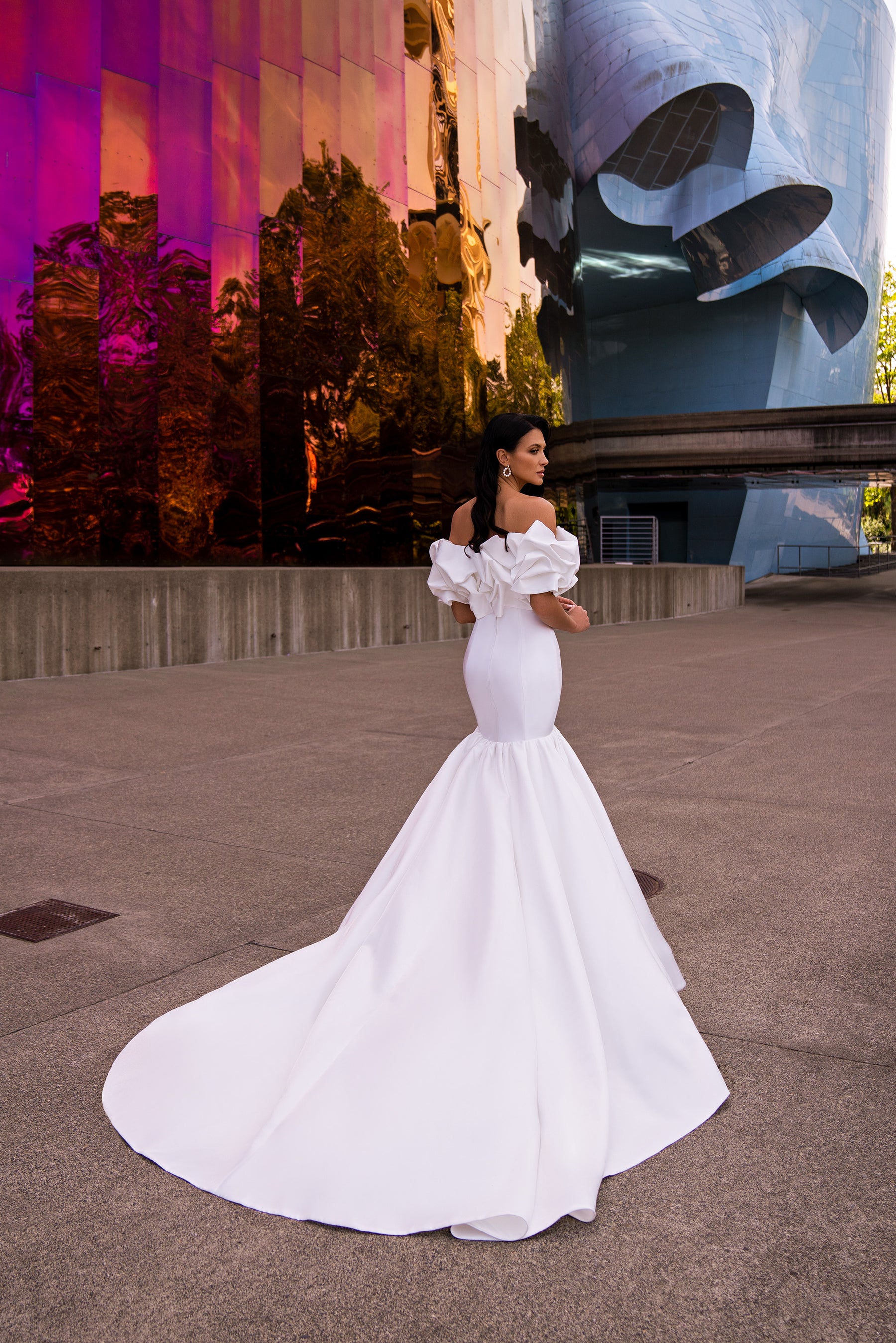 Side view of a white mermaid wedding dress showing the fitted silhouette, ruffled shoulders, and long train