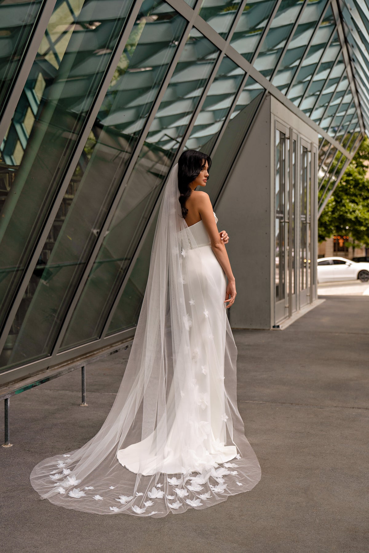 Open-back white wedding dress with a long sheer train and floral appliqué edging