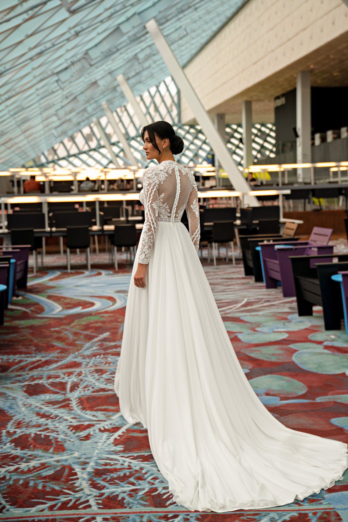 Ivory wedding dress showing its sheer lace back, long sleeves, flowing A-line skirt, and extended train