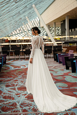 Ivory wedding dress showing its sheer lace back, long sleeves, flowing A-line skirt, and extended train