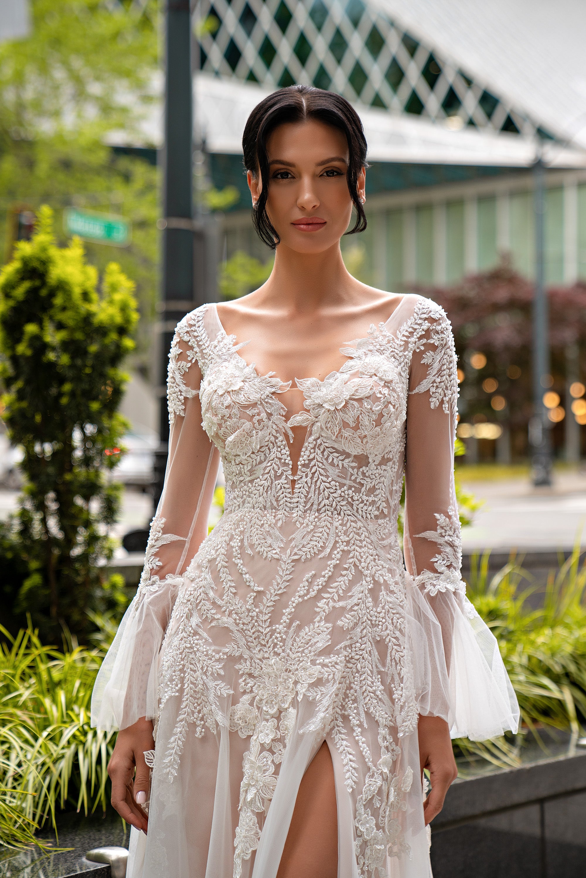 Close-up of an ivory wedding dress with sheer lace sleeves, floral appliqués, square neckline, and front slit