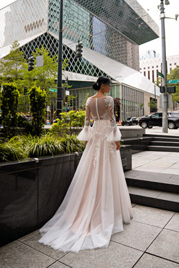 Open illusion-lace back and flowing train on an ivory wedding dress with long sheer sleeves
