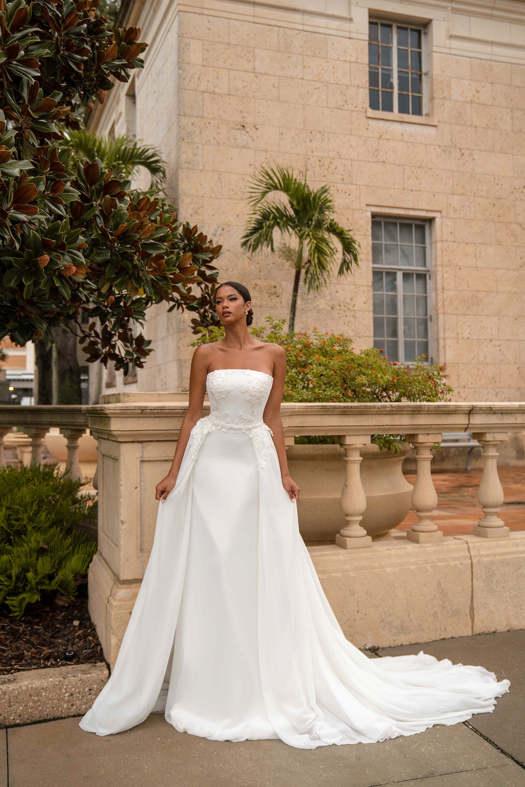 White strapless wedding dress with floral lace bodice, draped overskirt, and sweeping train