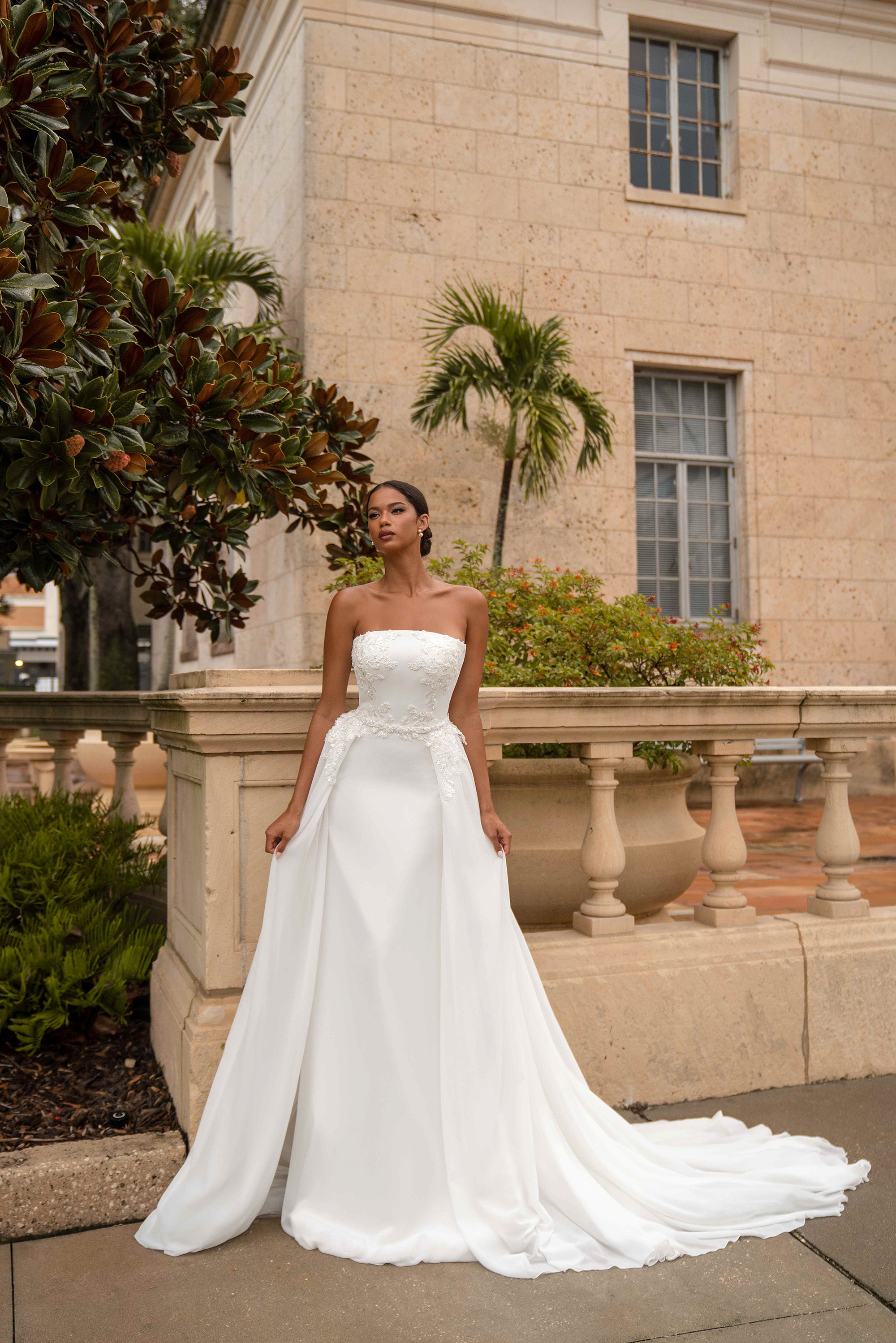 White strapless wedding dress with floral lace bodice, draped overskirt, and sweeping train