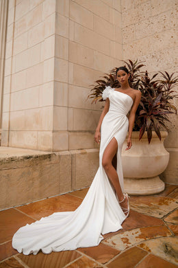 White asymmetrical wedding dress with a sculpted one-shoulder neckline, high slit, and sweeping train
